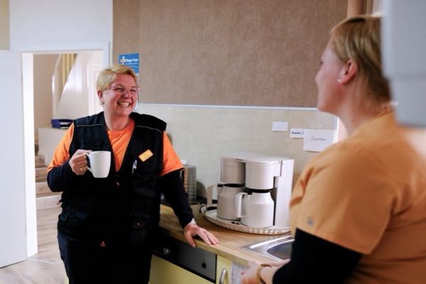 Zwei Kolleginnen lachen in der Büroküche bei einer Tasse Kaffee