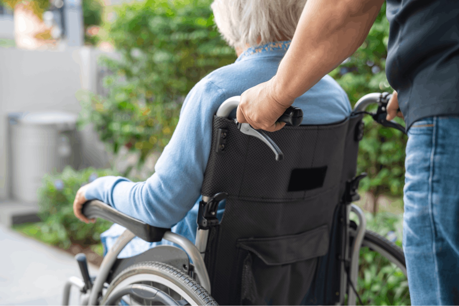 Ein älterer Mensch im Rollstuhl wird durch einen Garten geschoben