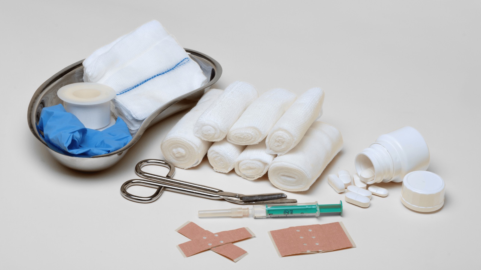 Verbandsmaterial, Einmalhandschuhe, Schere und Pflaster auf hellem Grund
