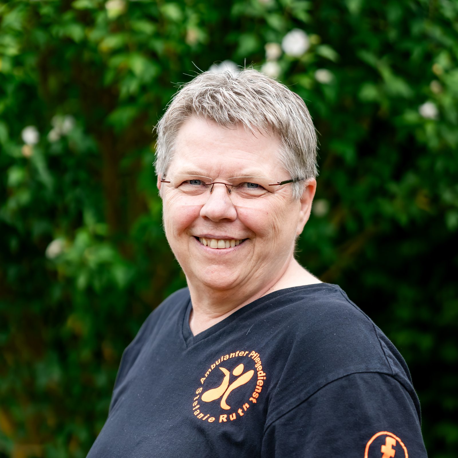 Stefanie Ruth, Inhaberin, in dunklem Dienstshirt im Garten, lächelt in die Kamera